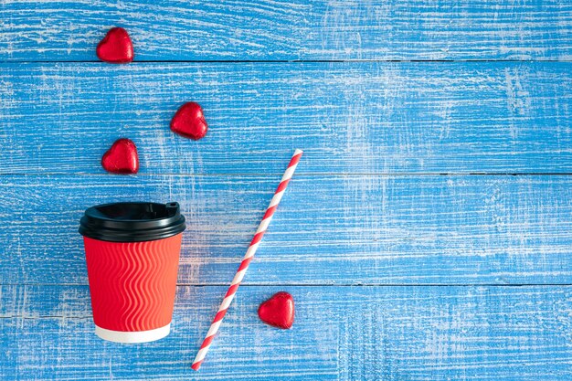 Photo gratuite une tasse de papier rouge et des bonbons en forme de cœur sur un fond en bois bleu