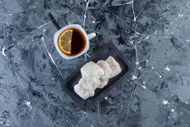 Tasse de thé au citron et assiette de barbe à papa sur une surface en marbre.