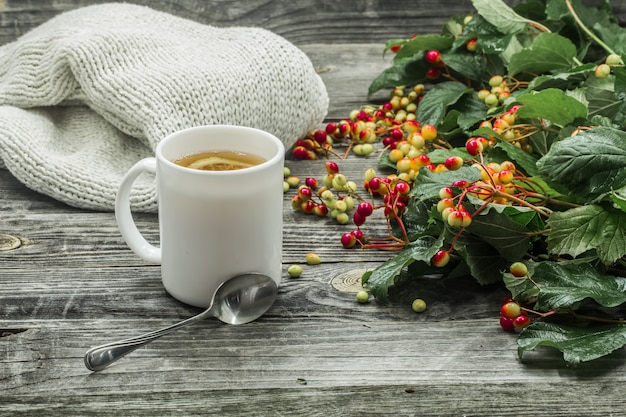 la tasse de thé sur un beau fond en bois avec pull d'hiver, baies, automne