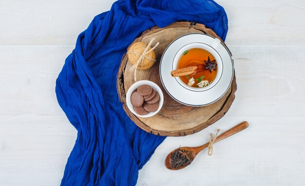 Tasse de thé, biscuits bruns et blancs sur planche de bois avec foulard bleu et une cuillère de clous de girofle