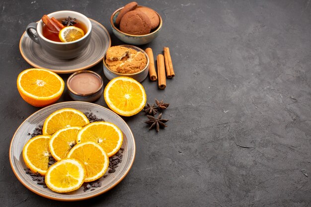 tasse de thé avec des biscuits et des oranges fraîches en tranches sur noir