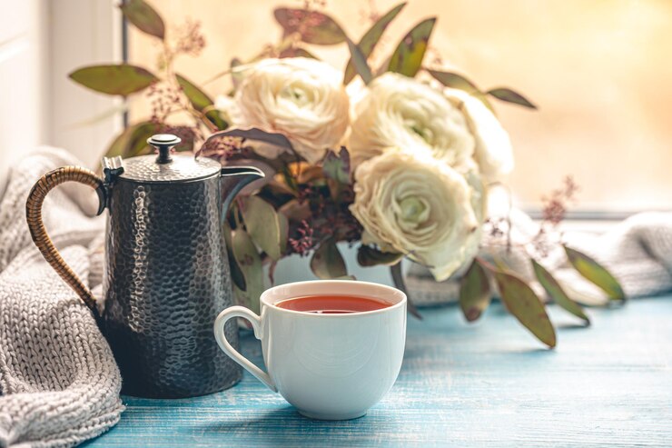 Photo gratuit une tasse de thé une bouilloire et des fleurs près de la fenêtre