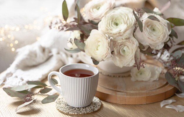 Photo gratuite une tasse de thé et un bouquet de fleurs de ranunculus sur un fond flou