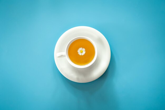 Une tasse de thé à la camomille sur fond bleu à plat