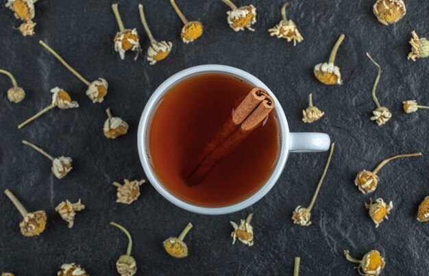 Tasse de thé à la cannelle et tas de camomille séchée.