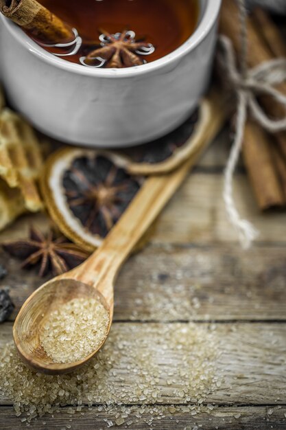 une tasse de thé chaud avec un bâton de cannelle et une cuillerée de cassonade sur bois