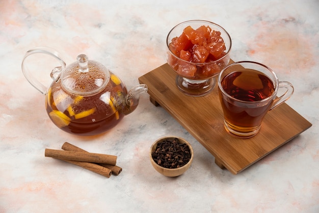 Tasse de thé chaud, théière et confiture de coings sucrés sur planche de bois.