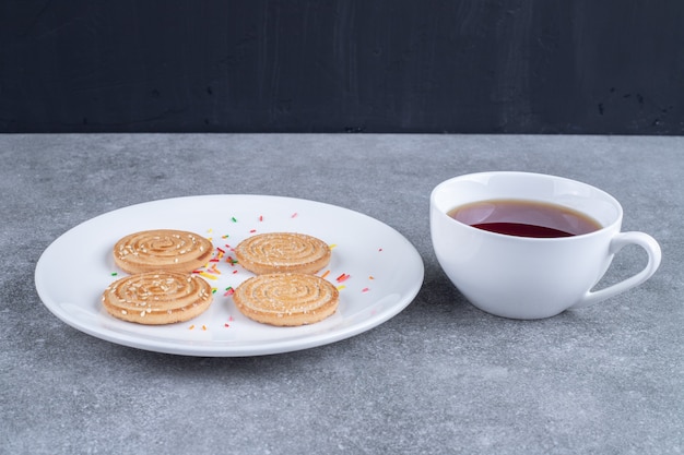 Tasse de thé et de délicieux biscuits sur plaque blanche