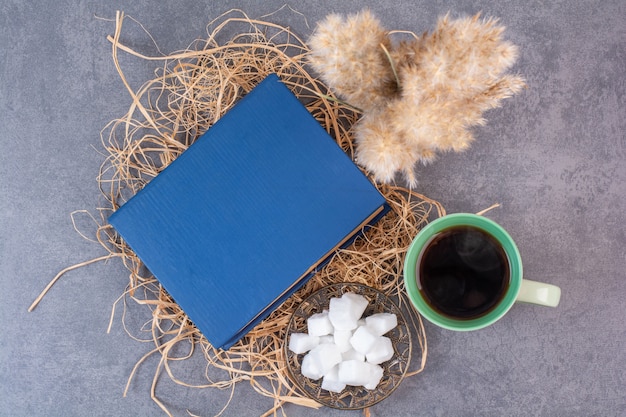 Une tasse de thé délicieux avec un livre et du sucre sur du foin.