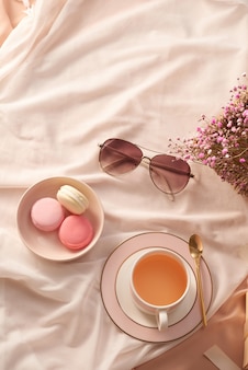 Tasse de thé, gâteau de macarons, verres et fleurs sur fond de tissu