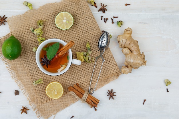 Tasse de thé, limes, une passoire à thé cannelle en napperon en lin avec gingembre sur surface grise