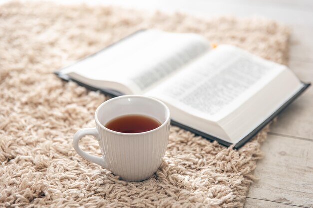 Photo gratuite une tasse de thé et un livre sur un tapis sur le sol dans une pièce en gros plan