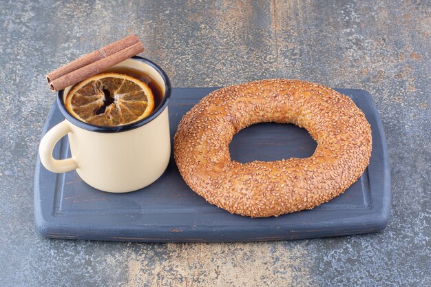 Tasse de thé en métal avec tranche de citron séchée bâton de cannelle et un bagel sur une planche sur une surface en marbre