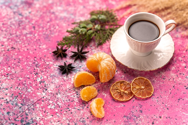 Tasse de thé à moitié supérieure avec des mandarines sur le bureau rose clair.