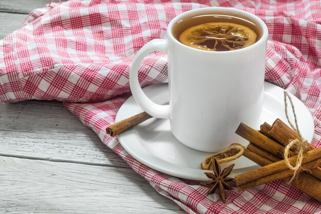 Tasse de thé sur une nappe rouge, beau fond en bois blanc, bâtons de cannelle, citron et baies