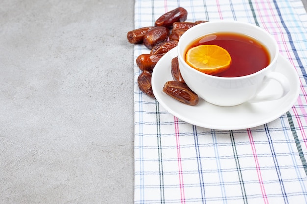 Une tasse de thé sur une soucoupe à côté des dates sur une serviette sur fond de marbre.