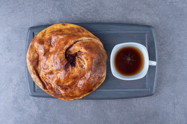 Une tasse de thé et de tarte sucrée sur un plateau en bois sur une table en marbre.