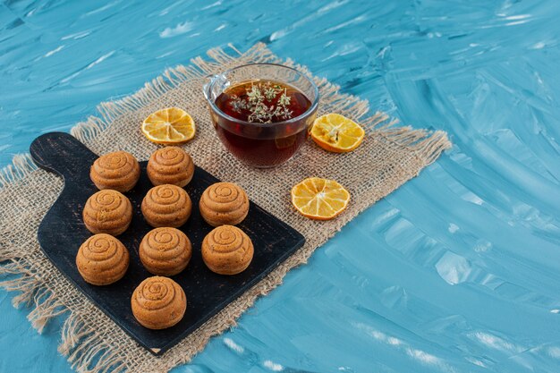 Une tasse de thé en verre avec des biscuits et des tranches de citron séchées sur un sac.