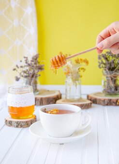 Tasse de thé en verre avec du tilleul dans des herbes biologiques naturelles et un pot de miel sur une table en bois blanc