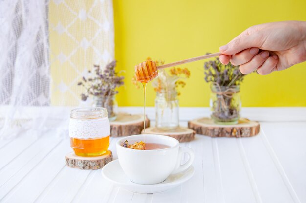 Tasse de thé en verre avec du tilleul dans des herbes biologiques naturelles et un pot de miel sur une table en bois blanc