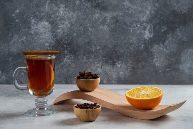 Une tasse de thé en verre avec une tranche d'orange et des thés en vrac séchés.