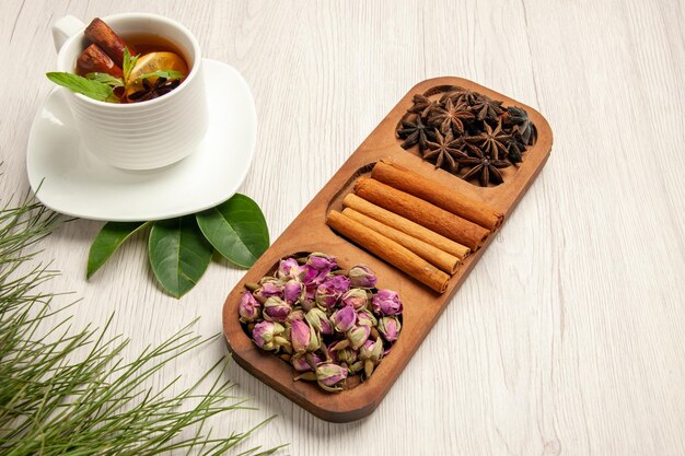 Tasse de thé vue à mi-hauteur avec de la cannelle et des fleurs sur une fleur de saveur de couleur de thé de bureau blanc