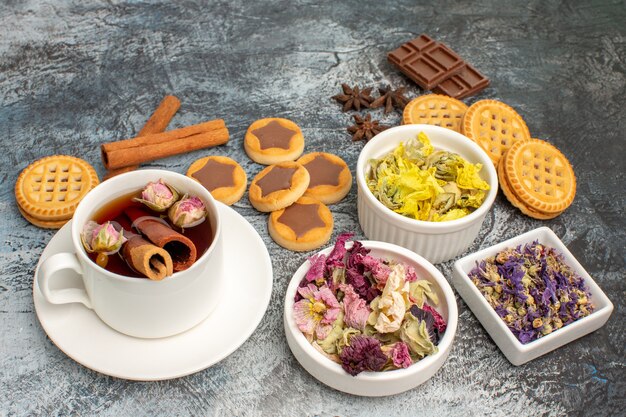 Tasse de tisane avec des biscuits et de la cannelle et des fleurs sèches sur fond gris