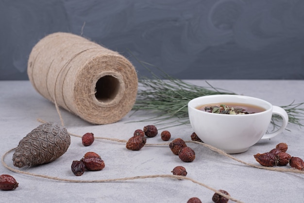 Tasse de tisane, canneberges séchées et pomme de pin sur table en marbre.