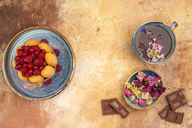 Une tasse de tisane chaude gâteau moelleux avec des fruits fleurs des barres de chocolat sur table de couleurs mixtes