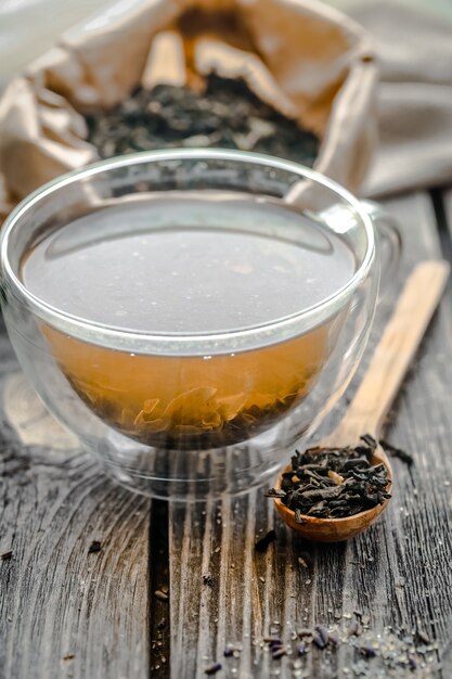 Tasse transparente de thé infusé avec des cuillères en bois adjacentes, du sucre et du thé sur fond de bois
