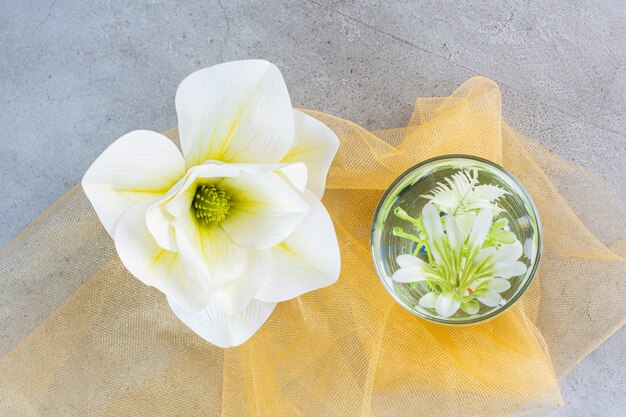 Une tasse en verre avec une belle fleur blanche sur une nappe jaune