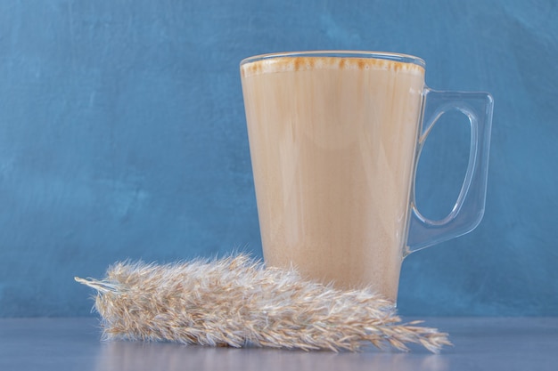 Tasse en verre de café au lait à côté de l'herbe de la pampa, sur la table bleue.