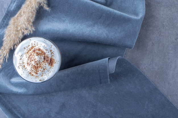 Tasse en verre de café au lait sur un morceau de tissu à côté de l'herbe de la pampa, sur la table bleue.