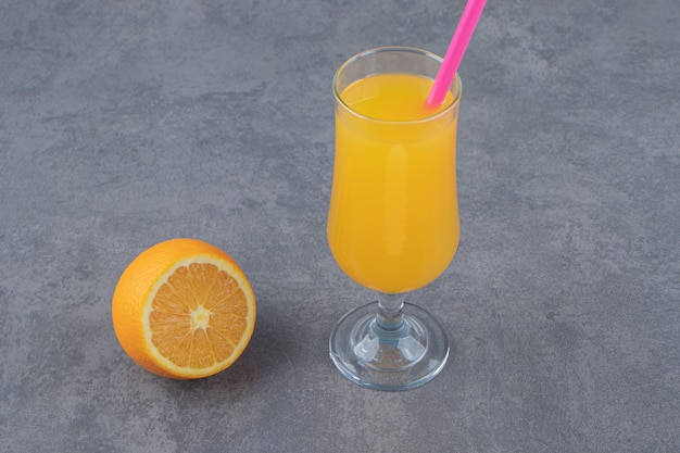 Une tasse en verre de jus d'orange frais avec une tranche d'orange et de paille