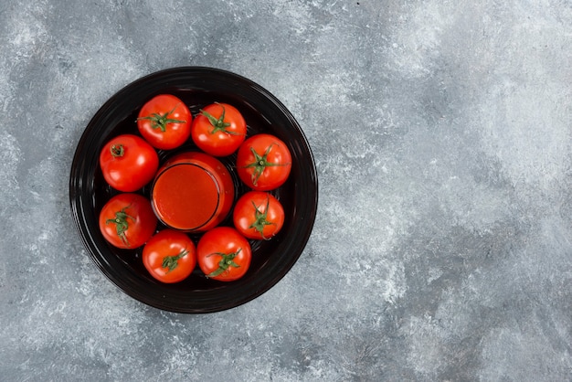Photo gratuite une tasse en verre de jus de tomate sur une plaque noire.