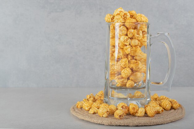 Tasse en verre plein sur un dessous de plat cerclé de pop-corn aromatisé au caramel sur une table en marbre.