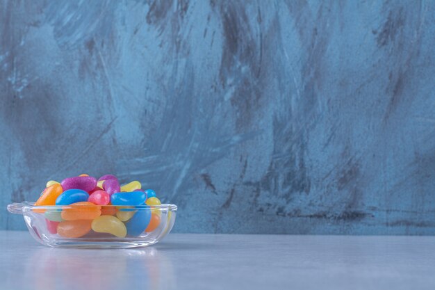 Une tasse en verre pleine de bonbons aux haricots colorés sur une surface grise.Photo de haute qualité