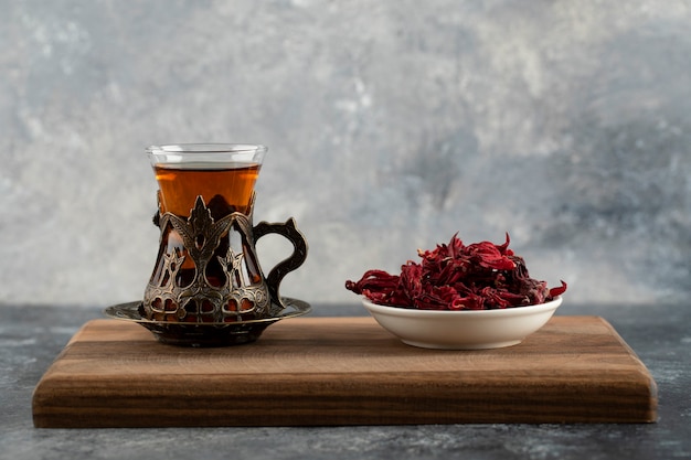 Une tasse en verre de thé chaud avec des fleurs séchées sur une planche à découper en bois.