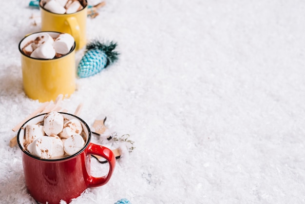 Tasses avec des bonbons près de jouets de Noël entre neige