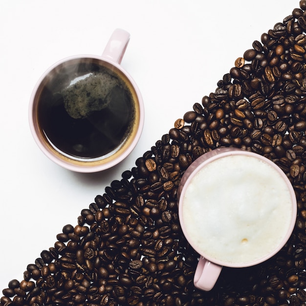 Tasses de café sur table blanche et tasse de lait sur table recouverte de grains de café