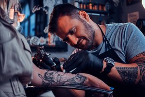 Un tatoueur concentré et diligent crée un nouveau tatouage sur la main d'une jeune femme au studio de tatouage.