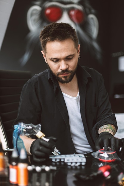 Tatoueur professionnel en gants noirs tenant une machine à tatouer à la main se préparant à faire un tatouage dans un studio moderne