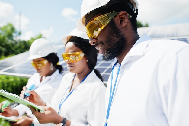 Un technicien afro-américain vérifie l'entretien des panneaux solaires Groupe de trois ingénieurs noirs réunis à la station solaire