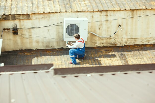 Technicien HVAC travaillant sur une pièce de condensateur pour unité de condensation. Homme ouvrier ou réparateur en uniforme réparant et ajustant le système de conditionnement, diagnostiquant et recherchant des problèmes techniques.