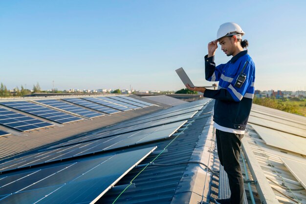 Technicien spécialisé ingénieur professionnel avec ordinateur portable et tablette vérifiant l'entretien de l'installation d'un panneau de toit solaire sur le toit de l'usine sous la lumière du soleil Ingénieurs tenant une tablette vérifiant le toit solaire