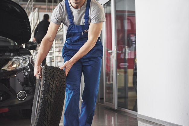 Technicien avec un vêtement de travail bleu, tenant une clé et un pneu tout en montrant le pouce vers le haut.