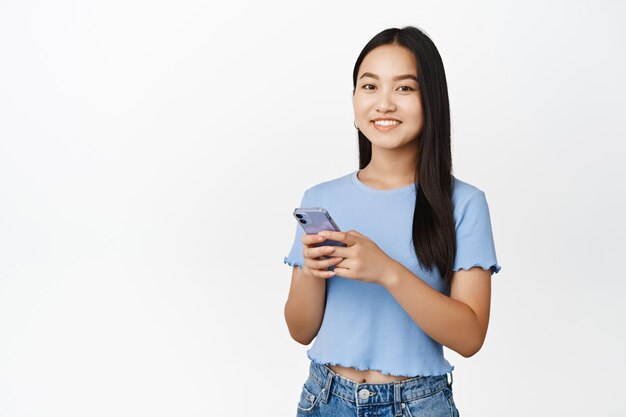 Technologie cellulaire Jeune fille asiatique souriante tenant un smartphone et regardant la caméra avec plaisir à l'aide d'une application mobile fond blanc