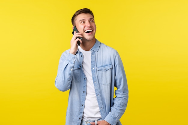 Technologie, concept de mode de vie. Joyeux bel homme souriant ayant une conversation heureuse au téléphone, appelant un ami, l'air enthousiaste et tenant un smartphone près de l'oreille, fond jaune.