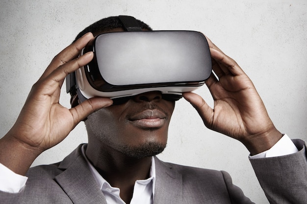 Technologie et divertissement. Employé de bureau à la peau sombre avec succès dans un élégant costume gris faisant l'expérience de la réalité virtuelle à l'aide de lunettes de casque VR.