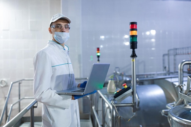 Photo gratuite un technologue avec un ordinateur portable dans ses mains fait une mise en place de la chaîne de production tout en se tenant au département de l'usine laitière